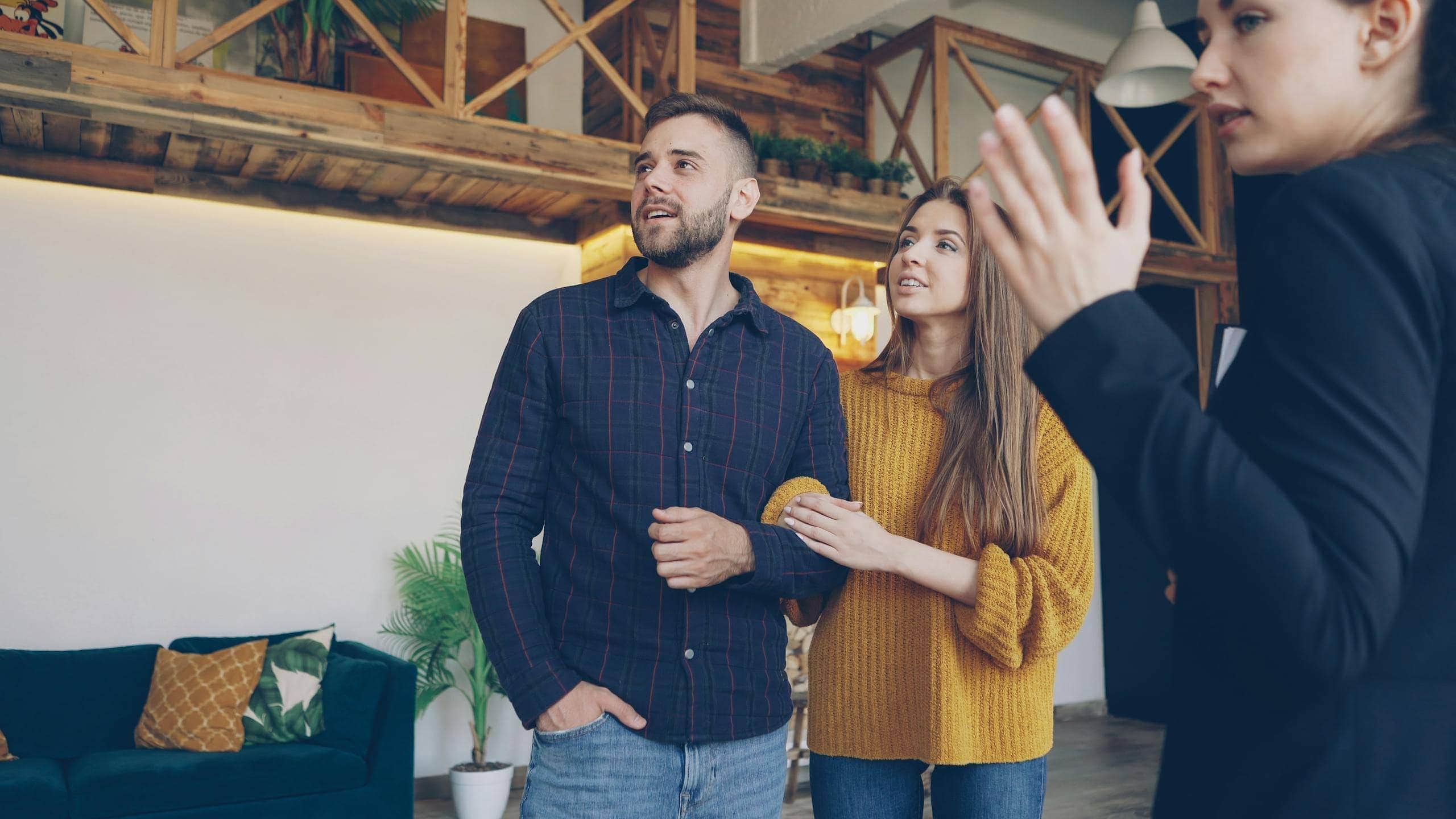 Jeune couple en visite immobilière avec une conseillère, intérieur lumineux et bois